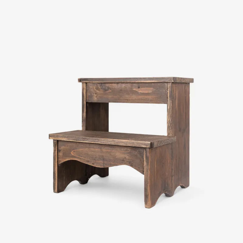 A rustic two-step wooden stool with a dark brown finish, featuring a small top step and a lower step with an arched opening, set against a plain light gray background.