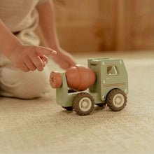 A child's hand pushing a small wooden toy cement mixer truck on a beige woven rug in a warm indoor setting.