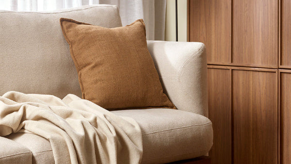 Cozy living room with beige sofa, brown pillow, and white blanket.