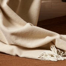 Beige blanket with tassels draped over a wooden surface